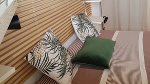 A bedroom with a wooden slatted headboard, a striped bedspread, and two pillows with floral patterns.
