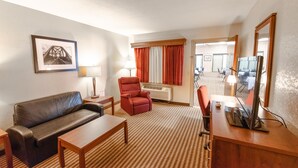 Una habitación de hotel con sofá, sillón, escritorio y un espejo grande.