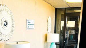 Un hall de hotel con mostrador de recepción, cartel de registro para huéspedes y una zona de estar con sofá y lámparas.
