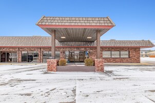 A building with a covered entrance, brick facade, and large windows.