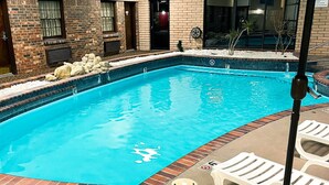 Una piscina con pared de ladrillo, sillas de descanso y una sombrilla.