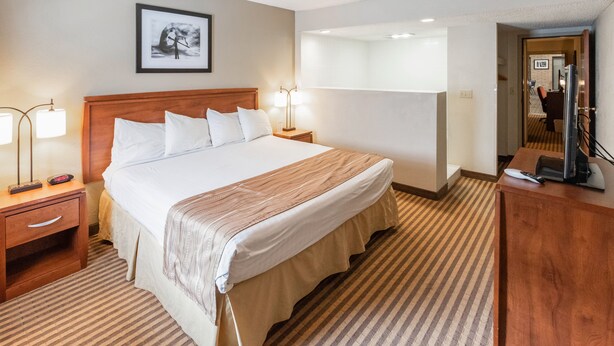 Una habitación de hotel con una cama grande, mesitas de noche, un escritorio y un espejo.