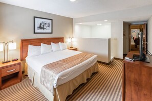 Una habitación de hotel con una cama grande, mesitas de noche, un escritorio y un espejo.