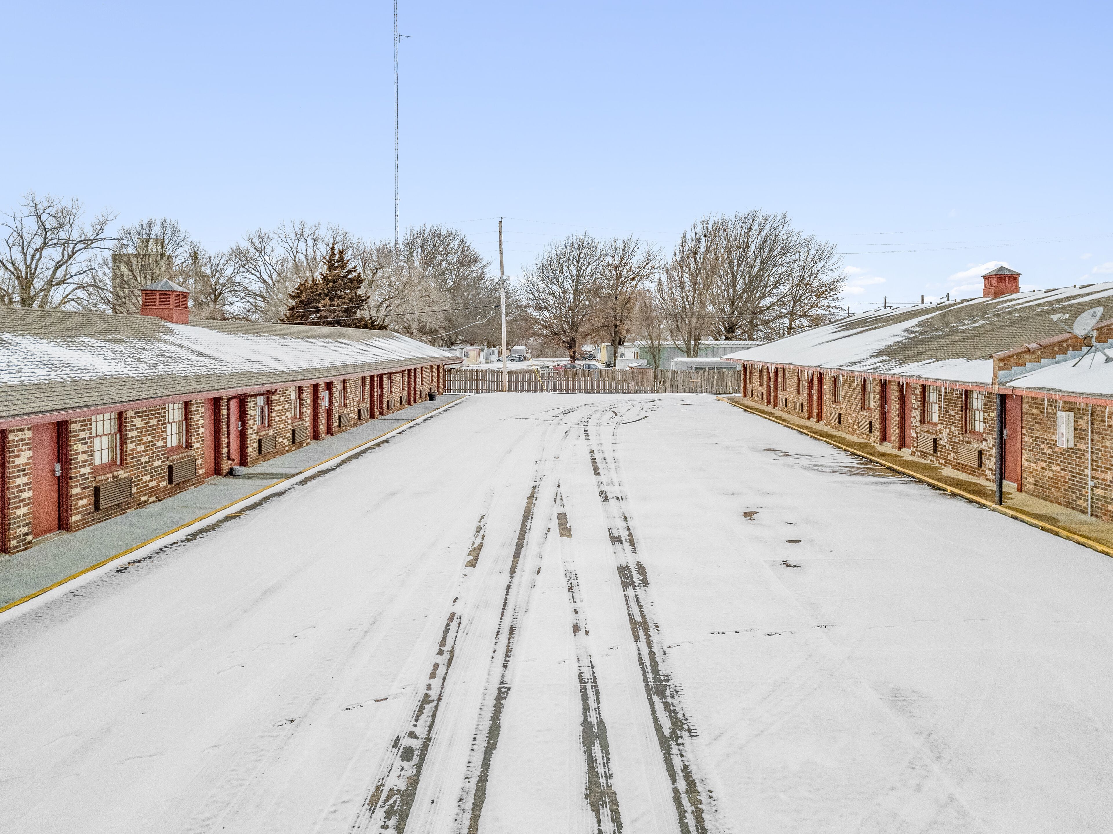 A snow-covered street with a row of brick buildings on either side, featuring a clear sky.