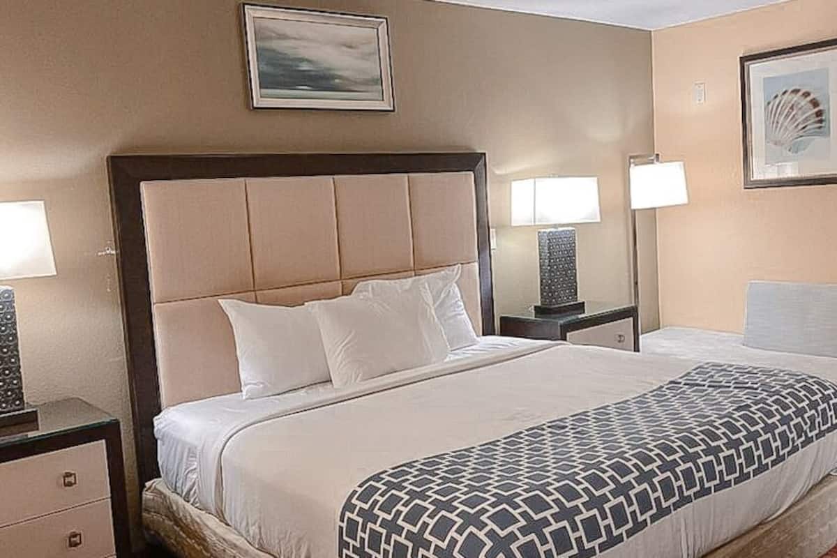 Una habitación de hotel con una cama grande, dos mesitas de noche, una silla y una lámpara de pared.