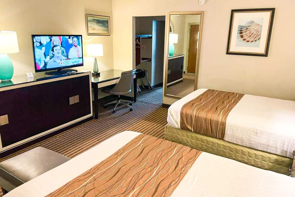 Habitación de hotel con dos camas, un escritorio con computadora, televisor y espejo.