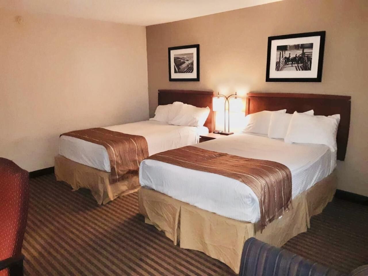 A hotel room with two beds, a nightstand with a lamp, and two framed pictures on the wall.