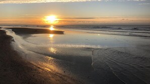 A beach at sunset with the sun reflecting on wet sand.