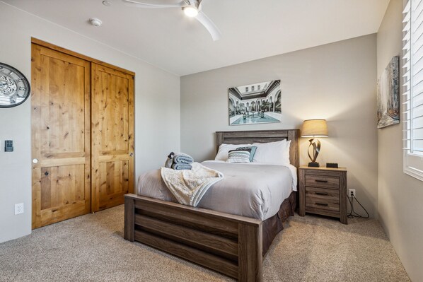 A bedroom with a wooden bed, a nightstand, a wall clock, and a large wooden door.
