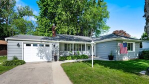 A single-story house with a garage, a front porch, and an American flag. - Three bedroom | 2 Bath Ranch Home Steps Away from the Water (Sturgeon Bay)