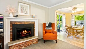 A living room with a fireplace, a dining area with wooden chairs, and a view through a glass door to an outdoor space. - Three bedroom | 2 Bath Ranch Home Steps Away from the Water (Sturgeon Bay)