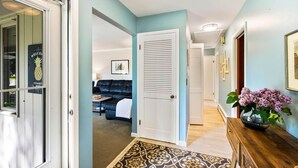 A hallway with a door leading to a living room, a wooden console table with a vase of flowers, and a patterned rug. - Three bedroom | 2 Bath Ranch Home Steps Away from the Water (Sturgeon Bay)