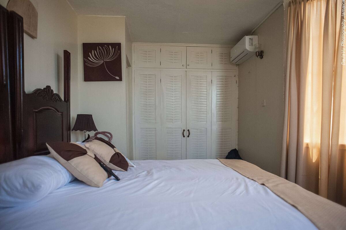 A hotel room with a bed, a wardrobe, a lamp, and a wall-mounted air conditioner.