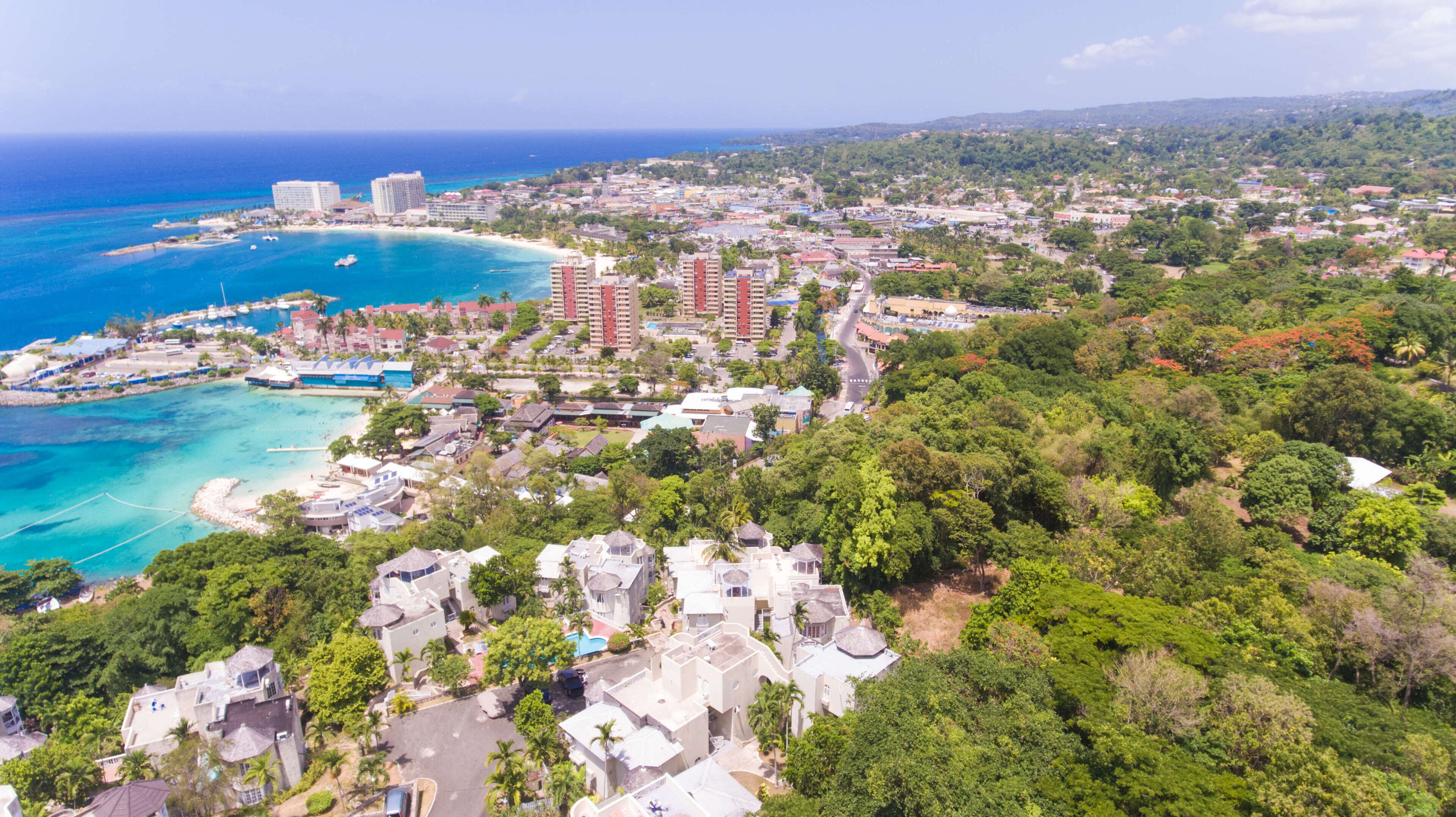 An aerial view of a coastal town with a beach, hotels, and lush greenery.