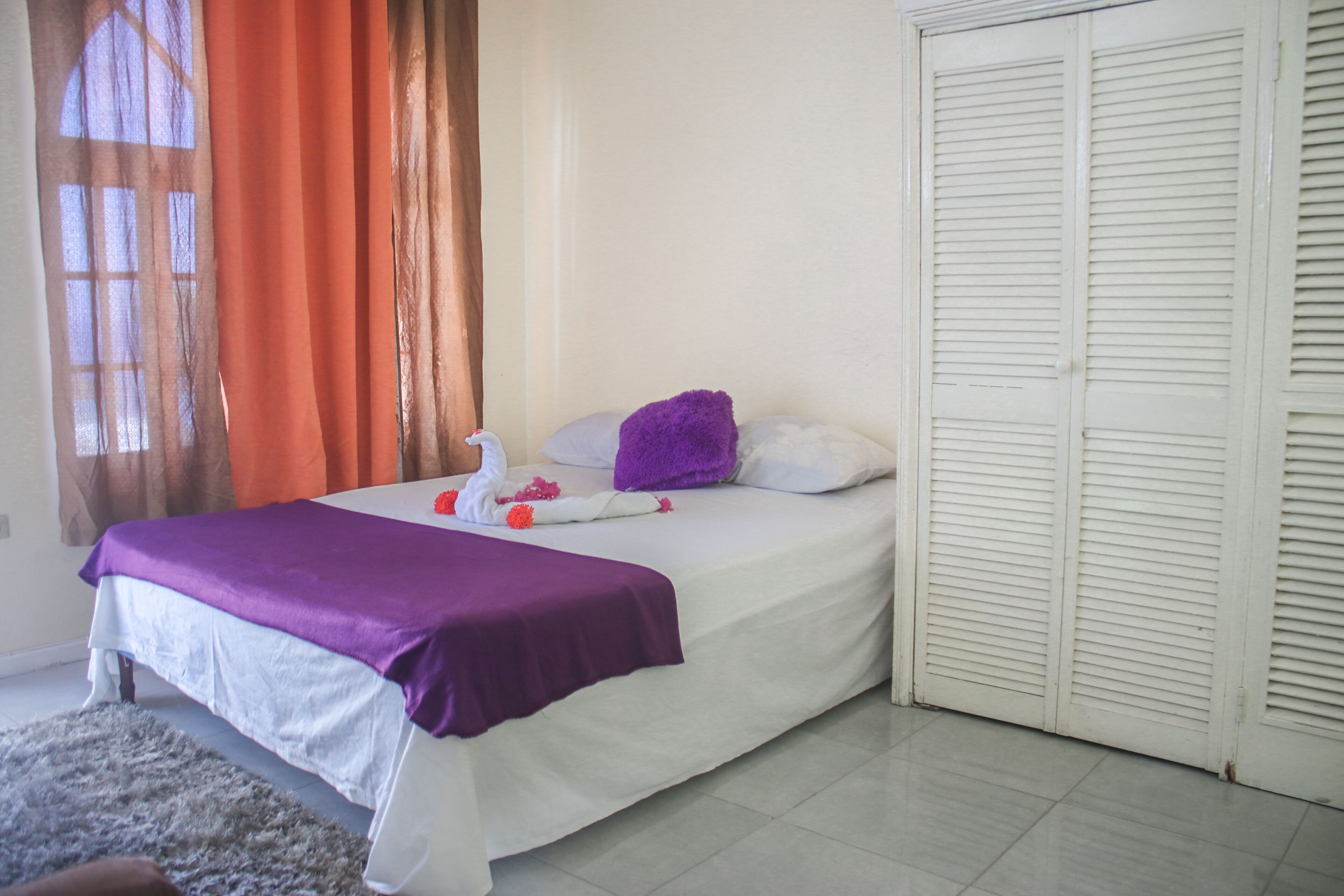 A hotel room with a bed, a purple blanket, a white pillow, and a white door.