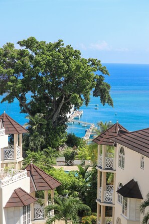 Un hotel frente al mar con varias construcciones, un árbol grande y vistas al océano.