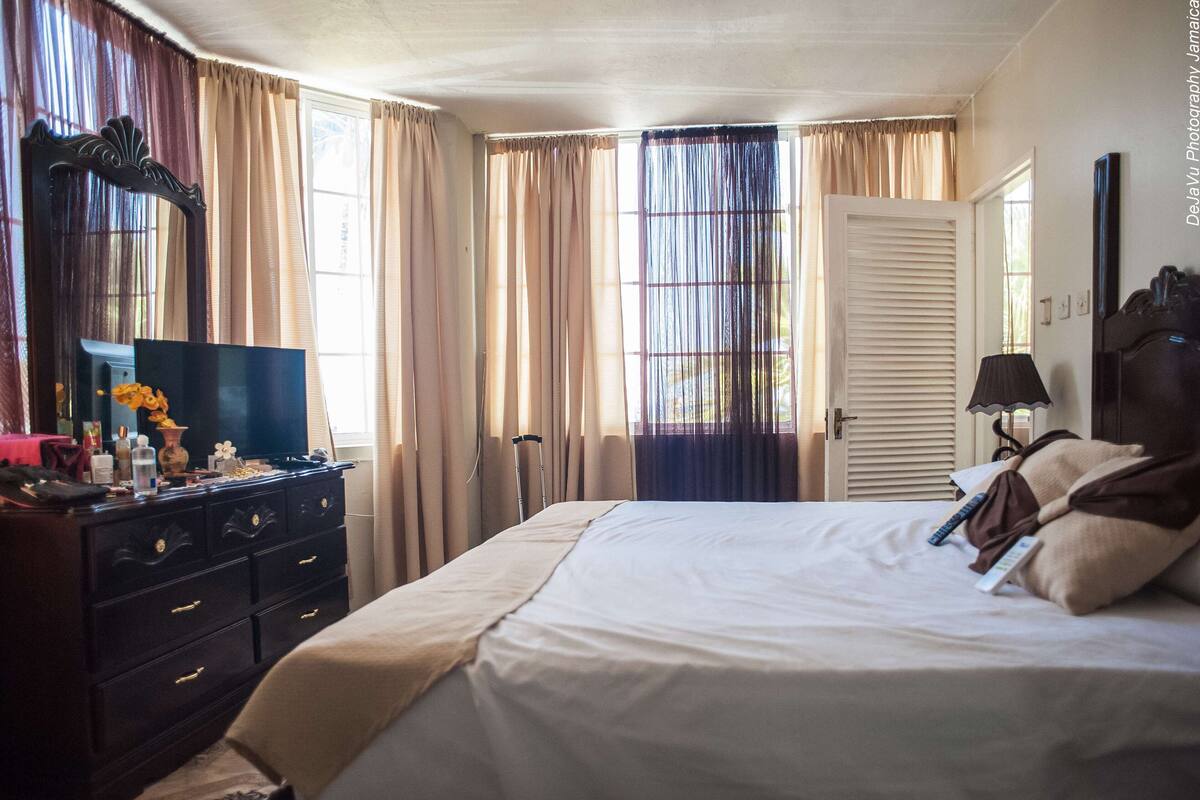 A hotel room with a bed, dresser, TV, and curtains.