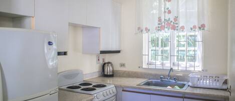 A kitchen with a refrigerator, stove, oven, sink, and window with floral curtains.