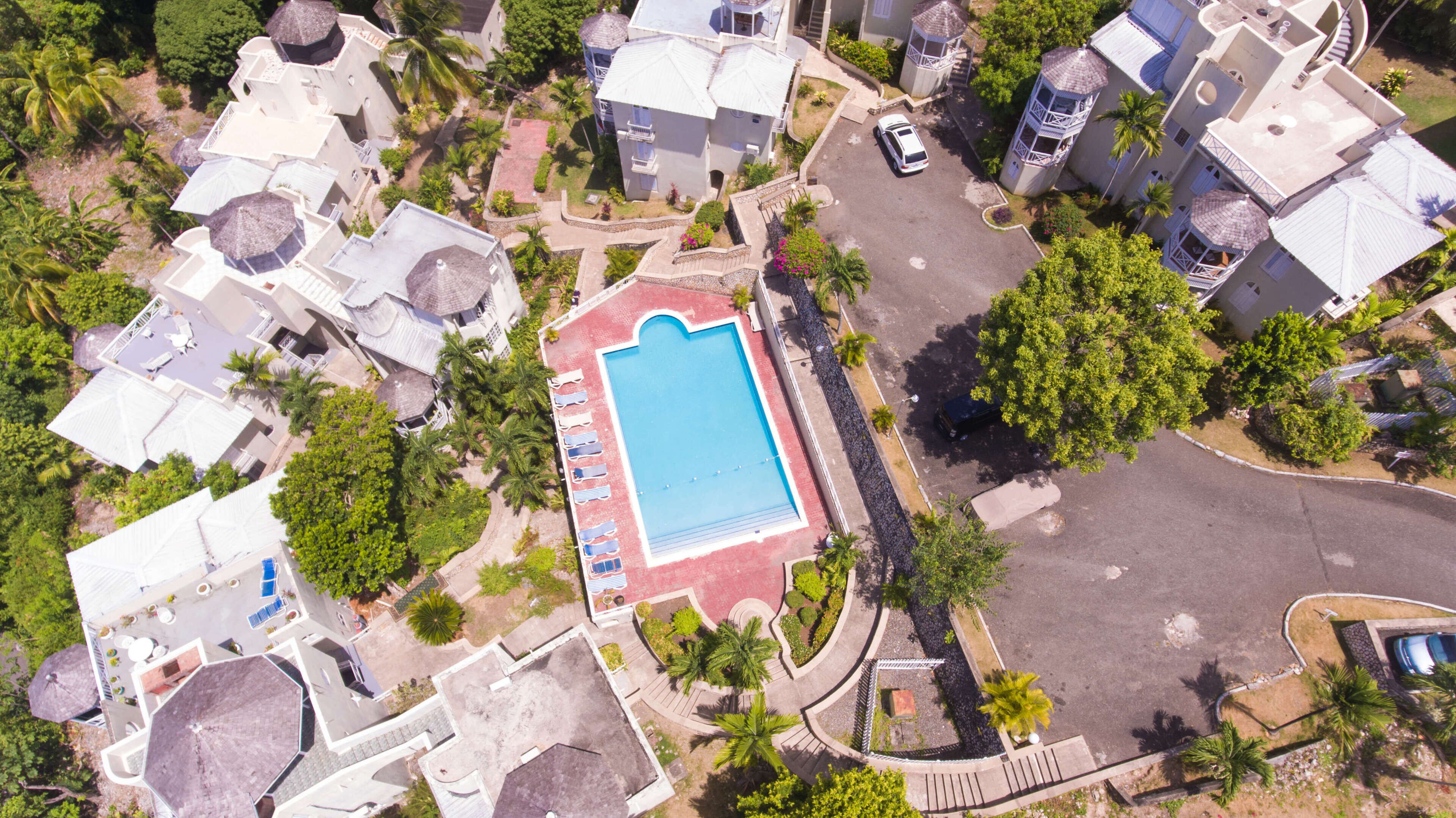 Luftaufnahme eines Resorts mit einem zentralen Schwimmbad, mehreren Villen und einem Parkplatz.