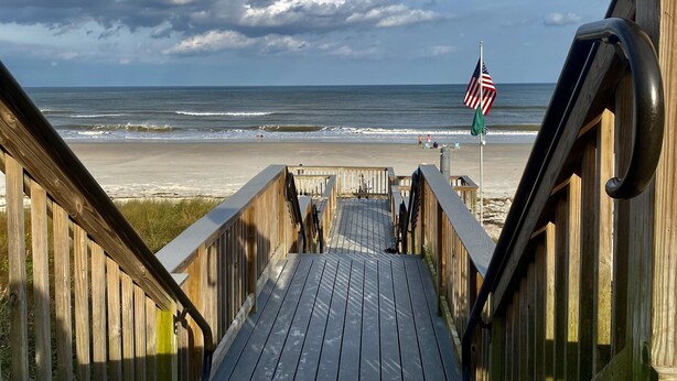 A wooden boardwalk leading to a beach with an American flag.