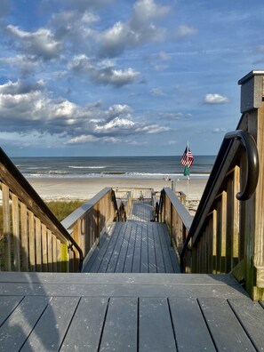 En træpromenade der fører til en strand med et amerikansk flag.