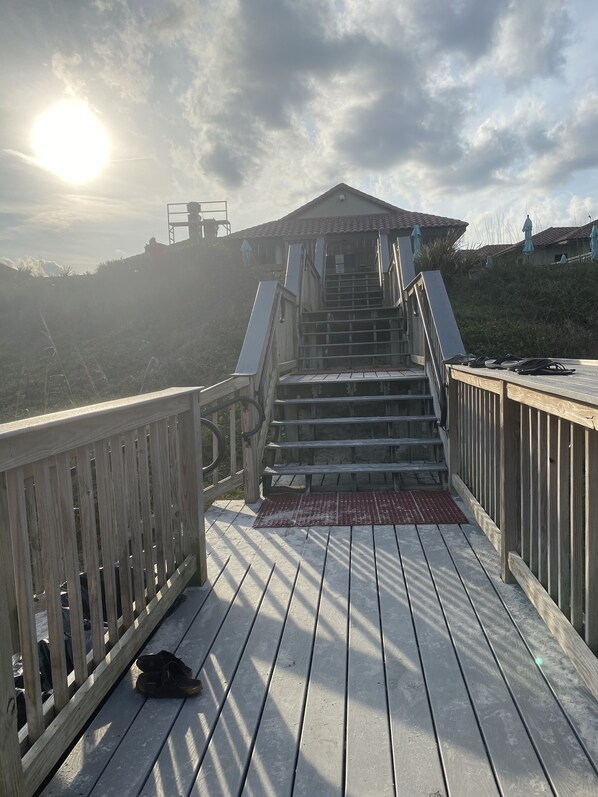 A wooden staircase leading up to a building with a tiled roof, surrounded by a wooden deck and railings.