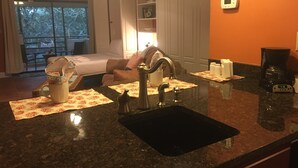 A hotel room with a kitchen area, a bed, a dining table, and a view of the outdoors.