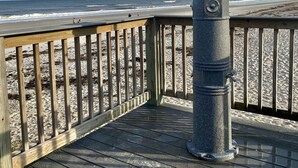 A wooden deck with a metal bollard, overlooking a sandy beach and ocean.