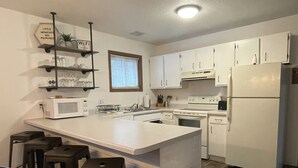 Een moderne keuken met witte kasten, een centraal eiland met krukken, een magnetron en een koelkast.
