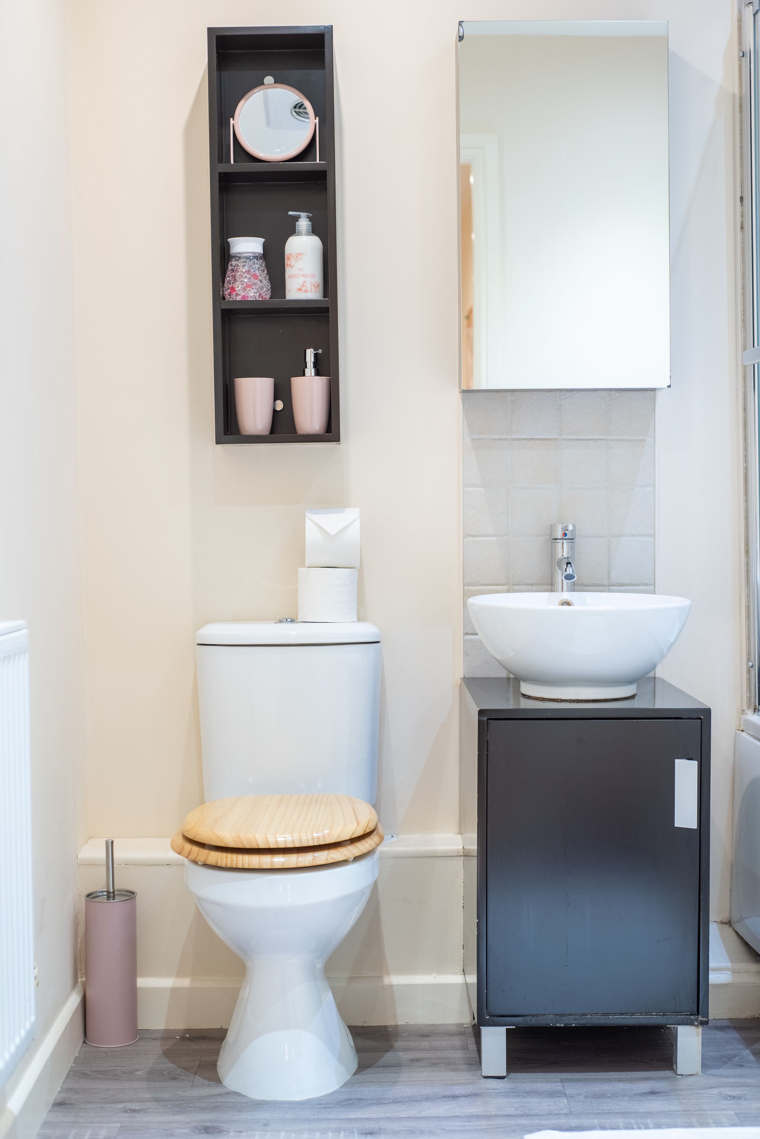 A bathroom with a toilet, a sink, a mirror, and a shelf with toiletries.