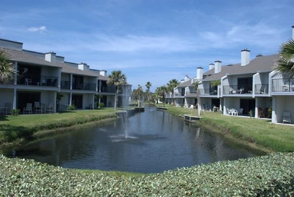 Un canal traverse un complexe hôtelier composé de bâtiments à plusieurs étages, chacun étant doté de balcons et d’espaces de détente en plein air.