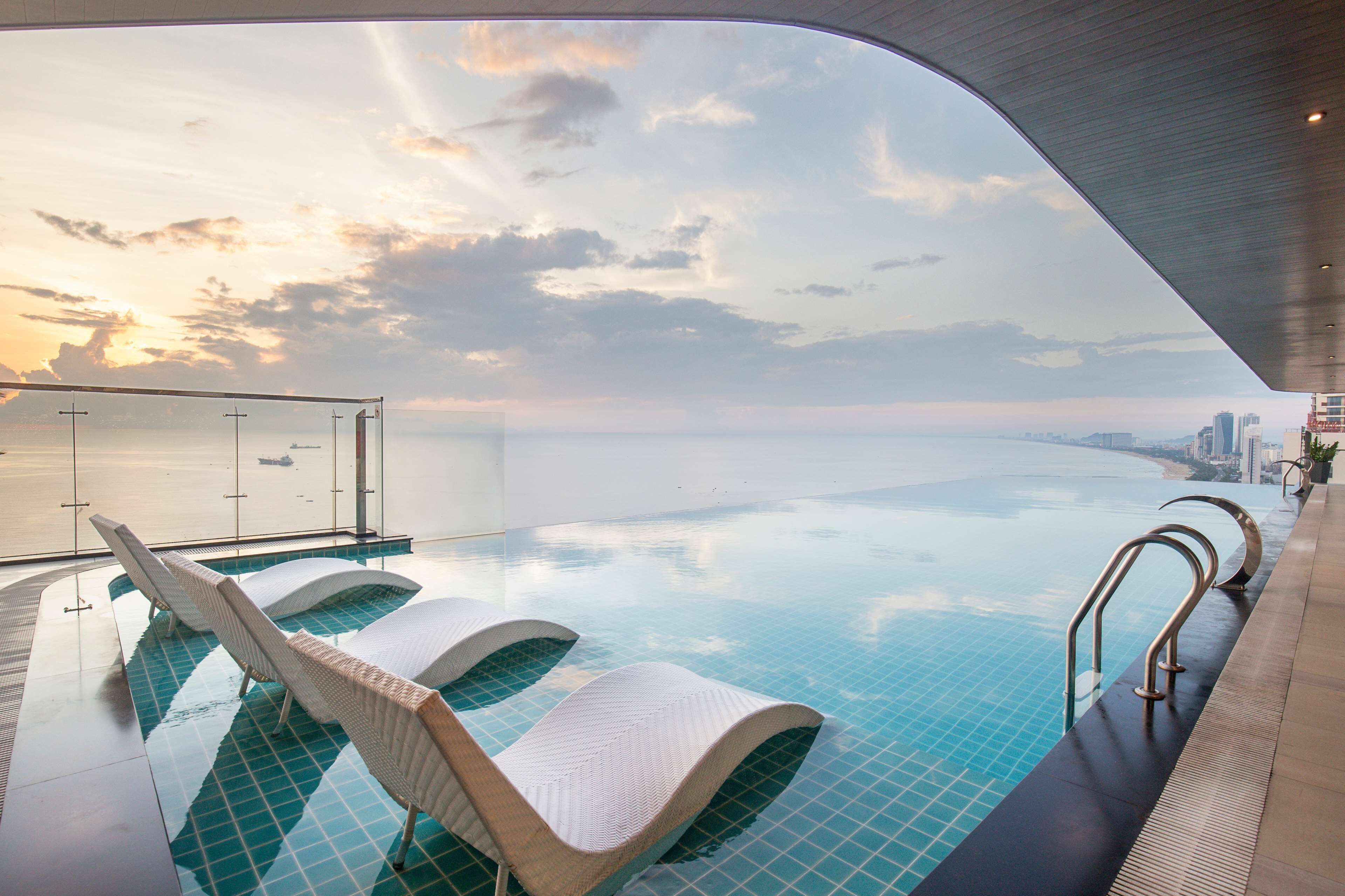 An infinity pool with lounge chairs and a view of the city skyline.