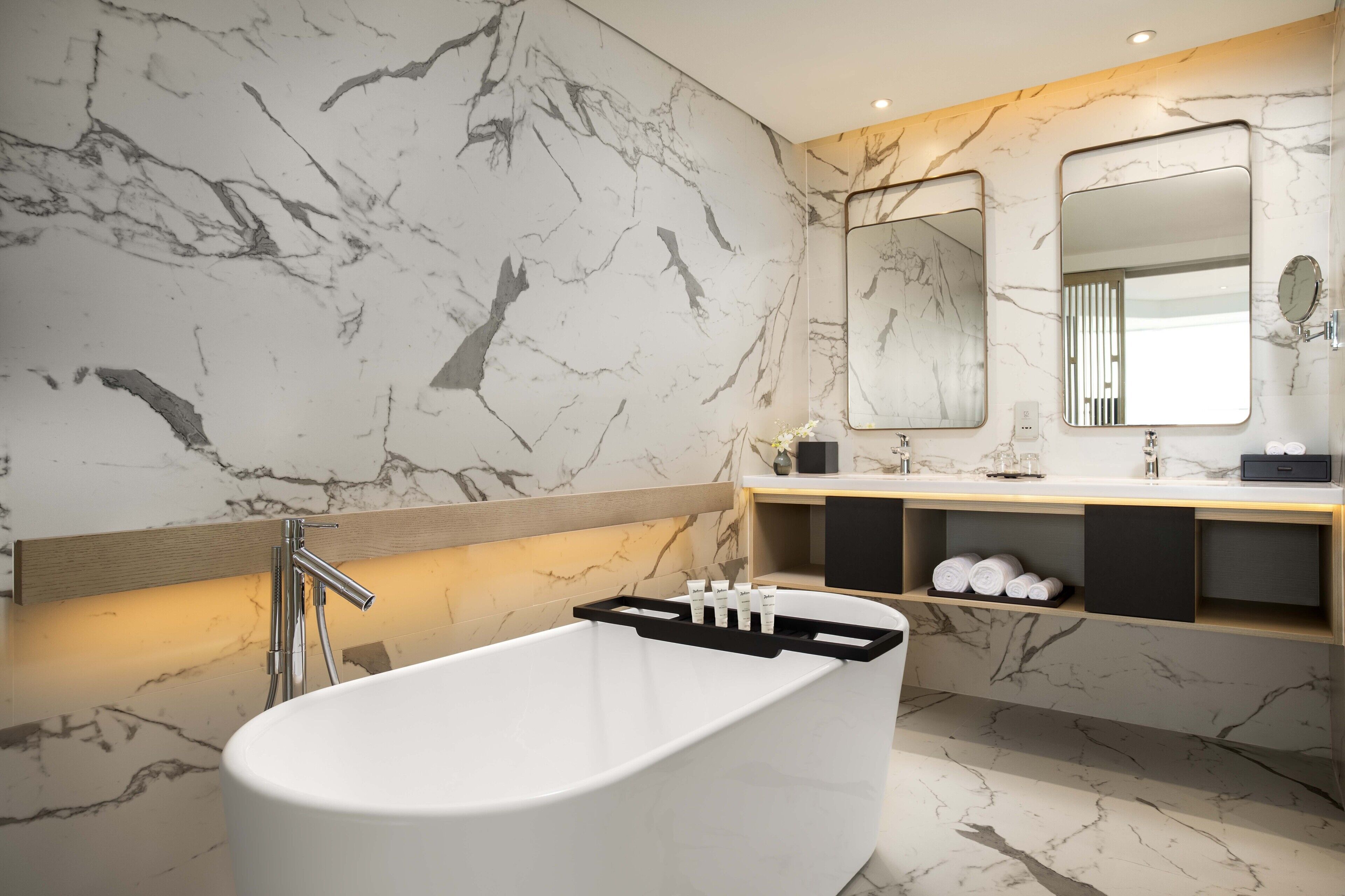 A modern bathroom with a freestanding bathtub, marble walls, and a vanity with a mirror and towel rack.