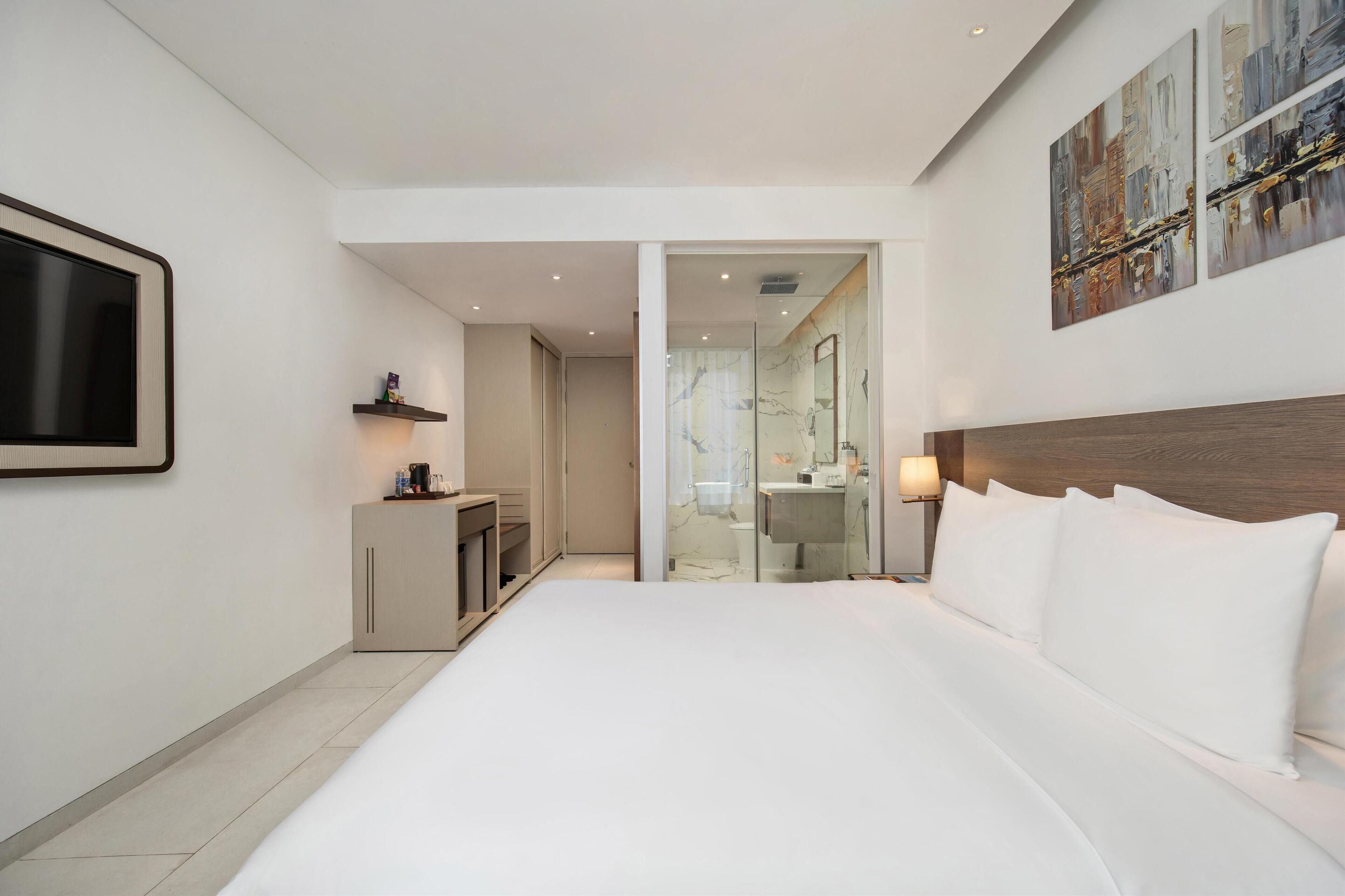 A modern hotel room with a large bed, a desk, and a bathroom visible through an open door.