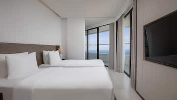 A hotel room with two beds, a large TV, and a balcony with a view of the sea.