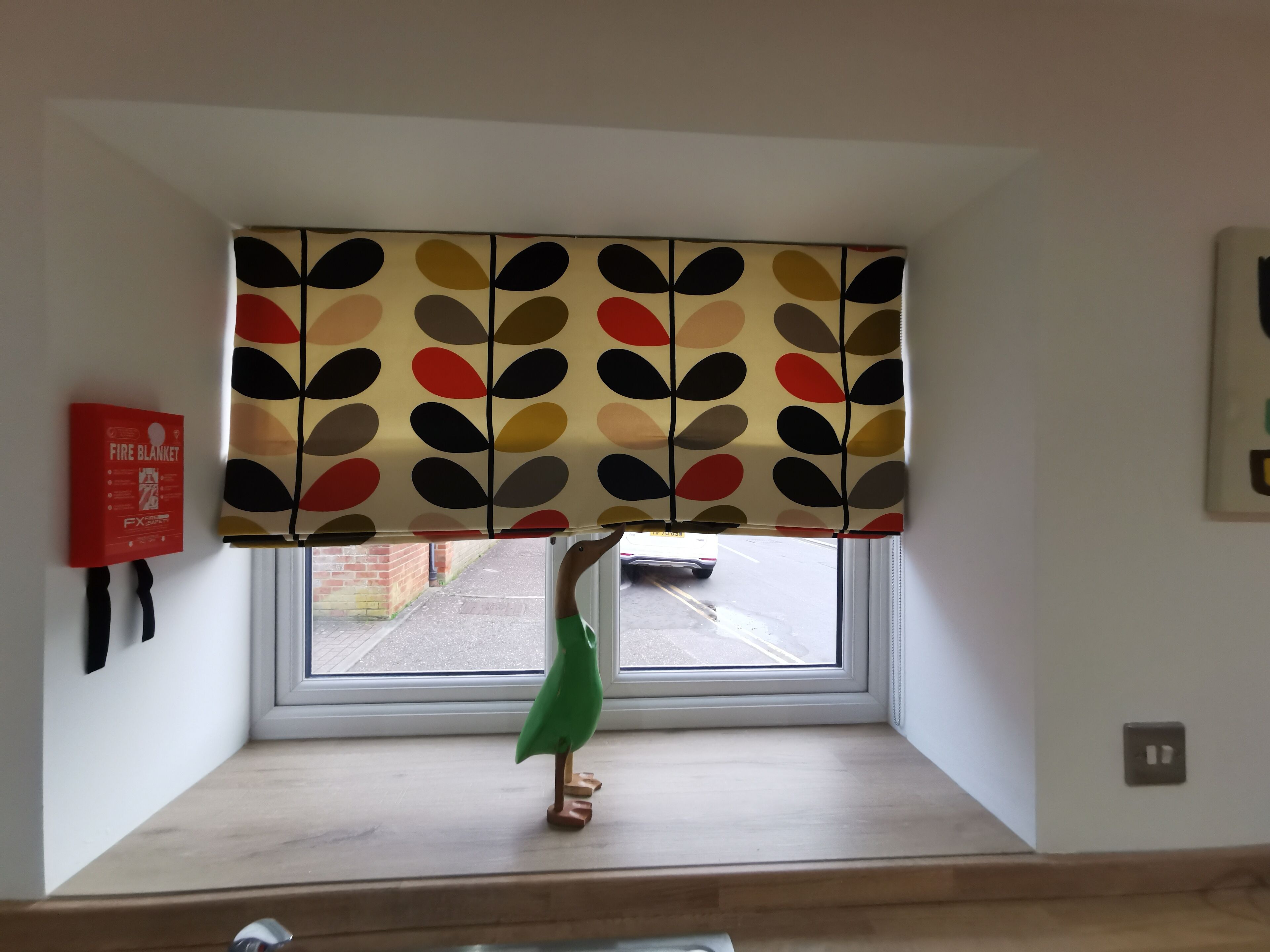 A room with a window, a fire blanket on the wall, and a green bird figurine on the windowsill.
