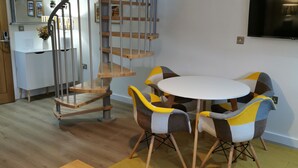 A modern kitchen with a built-in oven, a dining area with a round table and colorful chairs, and a spiral staircase leading to an upper level.