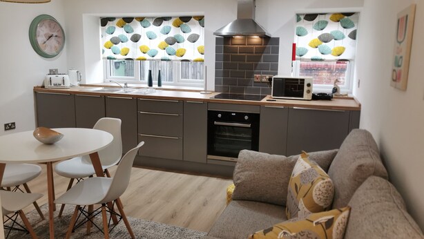 A modern kitchen with a central island, built-in oven, and a microwave. There is a dining area with a round table and chairs.
