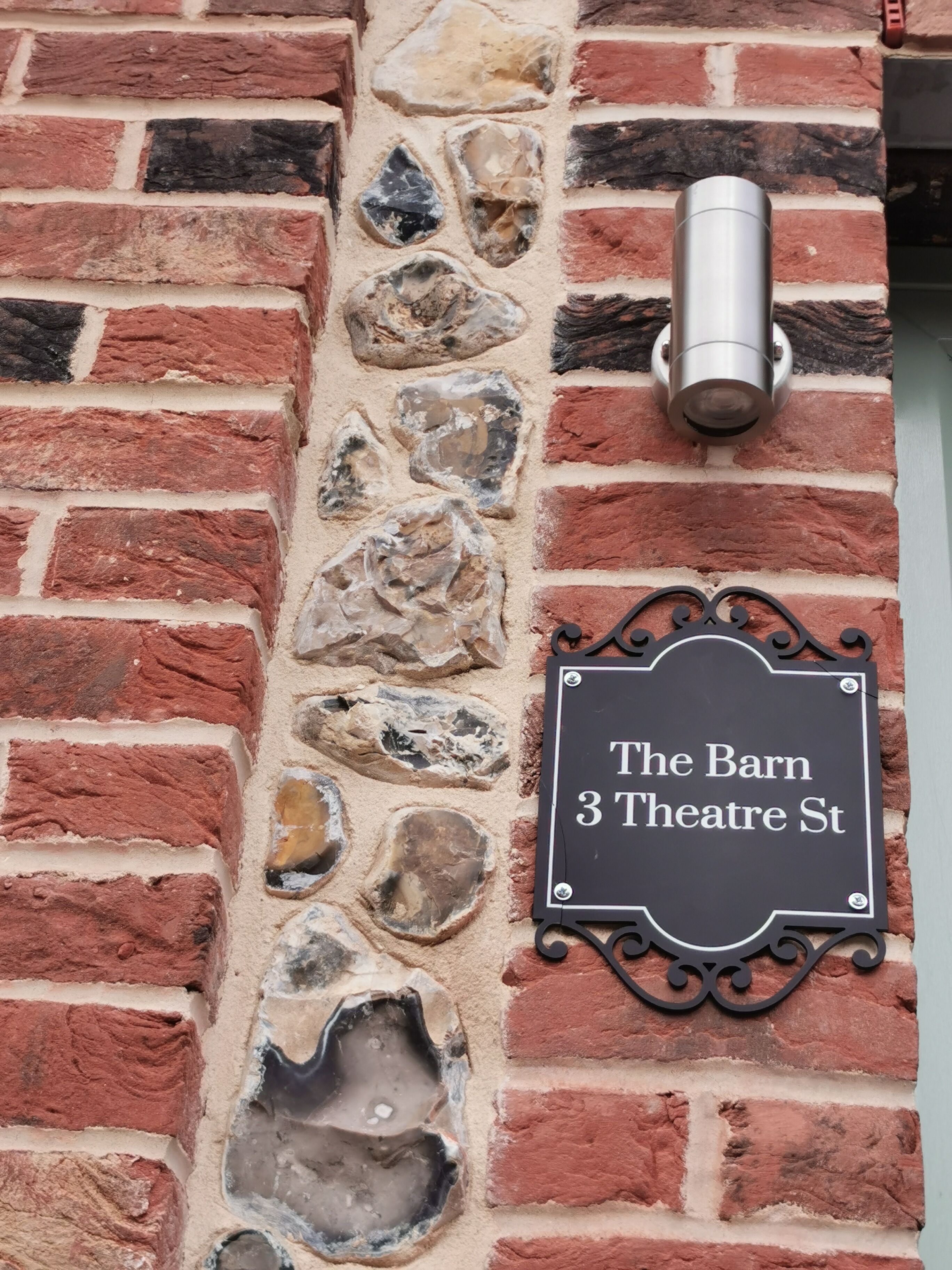 A brick wall with a stone pattern and a sign reading "The Barn 3 Theatre St".