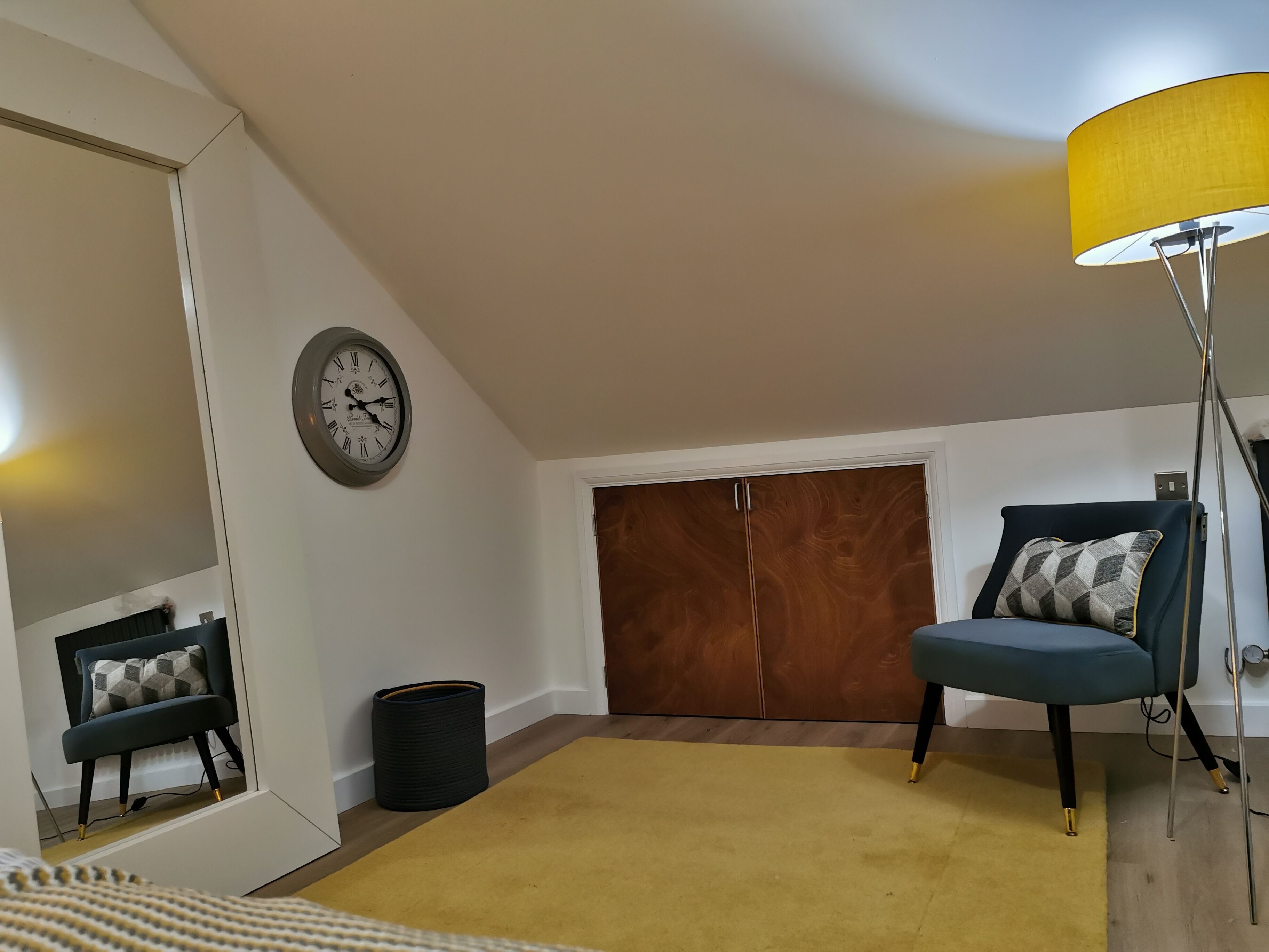 A room with a wooden wardrobe, a blue chair, a yellow lamp, and a clock on the wall.