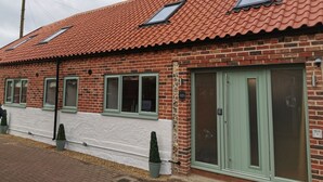 A brick building with a red-tiled roof, green-framed windows, and a green door.