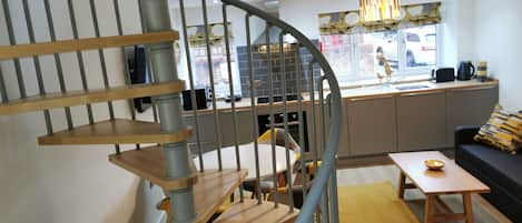 A modern kitchen with a curved staircase, a dining area with a table and chairs, and a sofa with cushions.