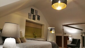 A bedroom with a bed, bedside table, lamp, window with blinds, and a mirror.