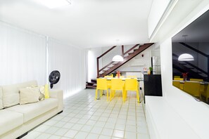 A modern living room with a sofa, a dining table with chairs, a staircase, and a kitchen area.