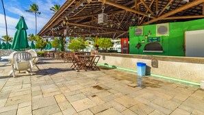 An outdoor patio with stone flooring, wooden tables and chairs, and green umbrellas. - Ancorar mar-piscina em Porto de Galinhas (Ipojuca)