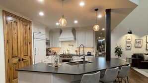 Een moderne keuken met een groot eiland, hangende lampen en een houten deur.