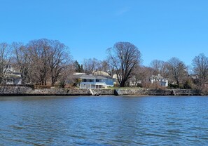 A waterfront property with a house featuring a balcony, a stone wall, and leafless trees.
