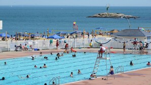 A swimming pool with multiple lanes, a lifeguard tower, and a view of the ocean.