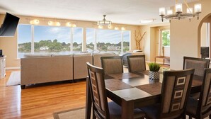 A dining area with a wooden table and chairs, a view of the outdoors, and a chandelier.