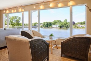 A room with a large window overlooking a lake, a sofa, two armchairs, and a small table with a plant.